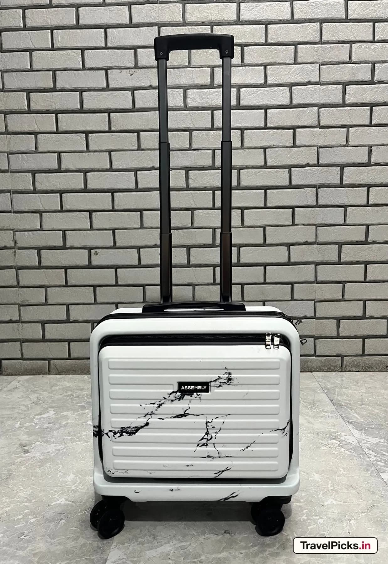 The white marble case standing against a brick wall with the handle extended.