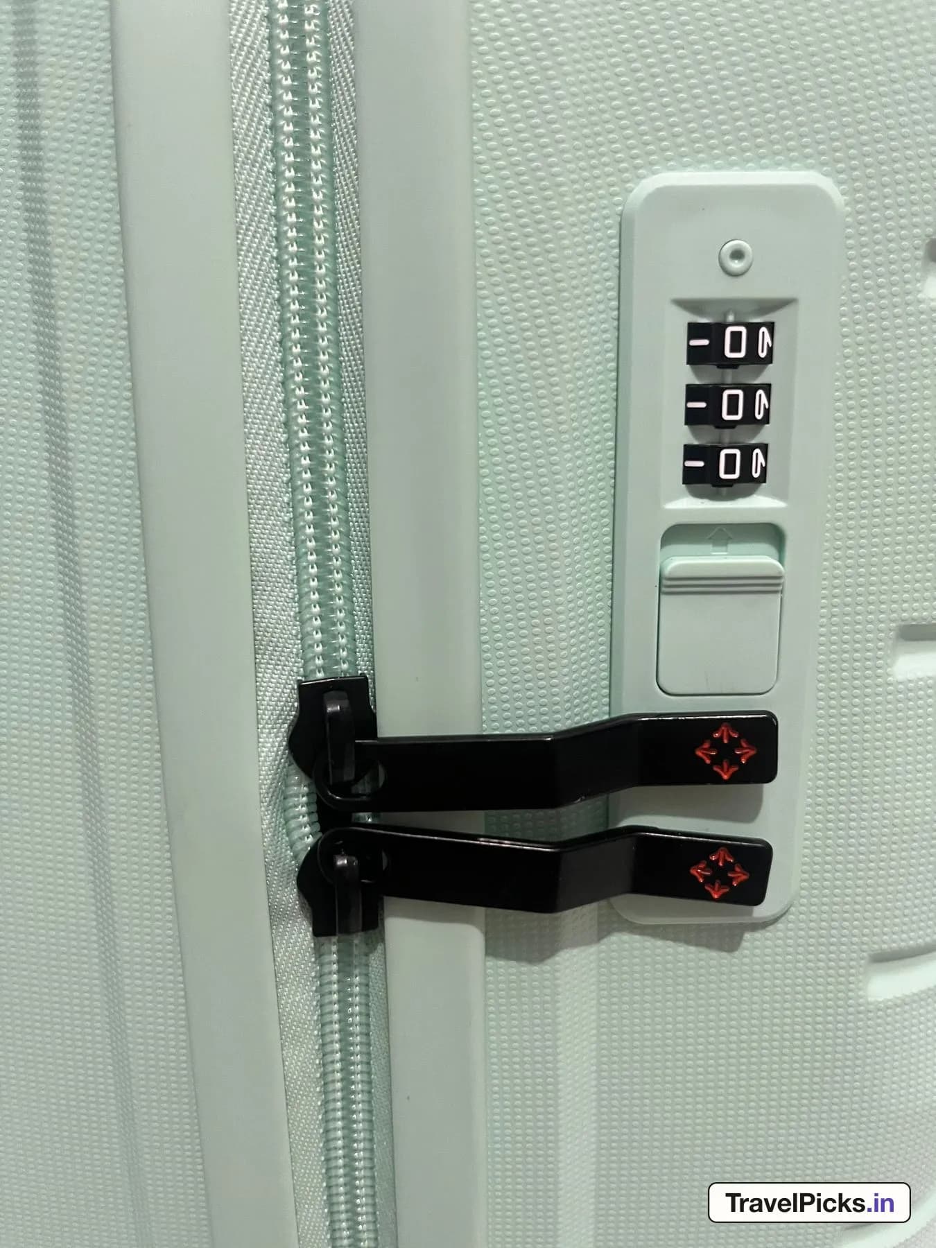 The lock panel on the side of the case: three black number dials, a mint slide button, and two black zip pullers docked below, each printed with an orange four-arrow logo.