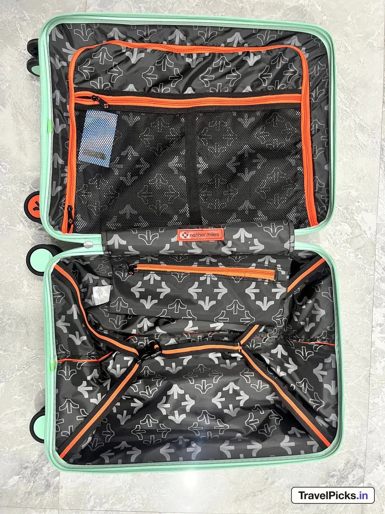 The case opened flat from above: a black lining printed with a grey arrow pattern, orange zips, a zipped divider with a mesh pocket in the lid, and cross-straps in the base.