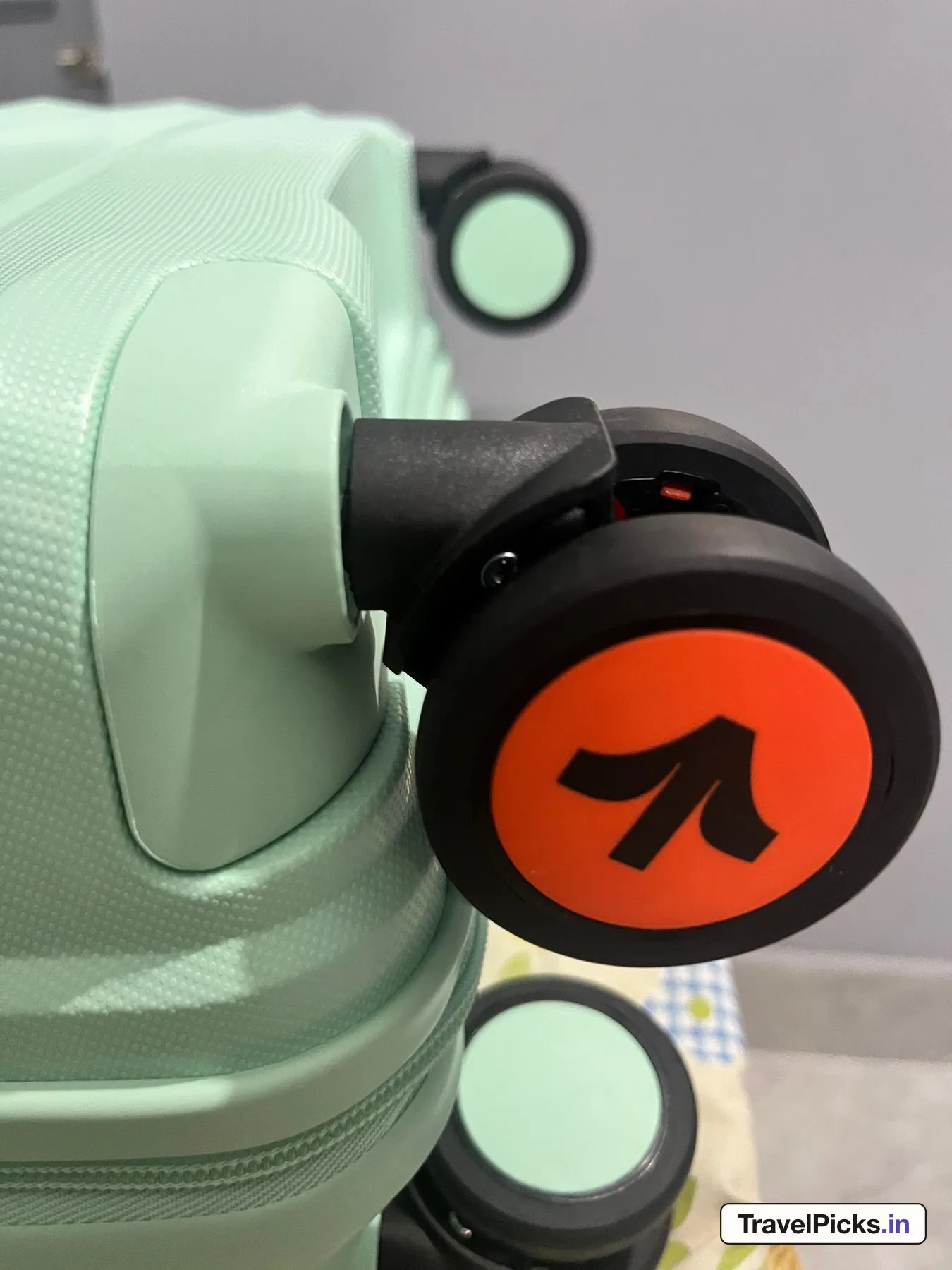 One corner of the case lying on its side, showing a double wheel with an orange hub on a black swivel, set into a raised block of the shell.