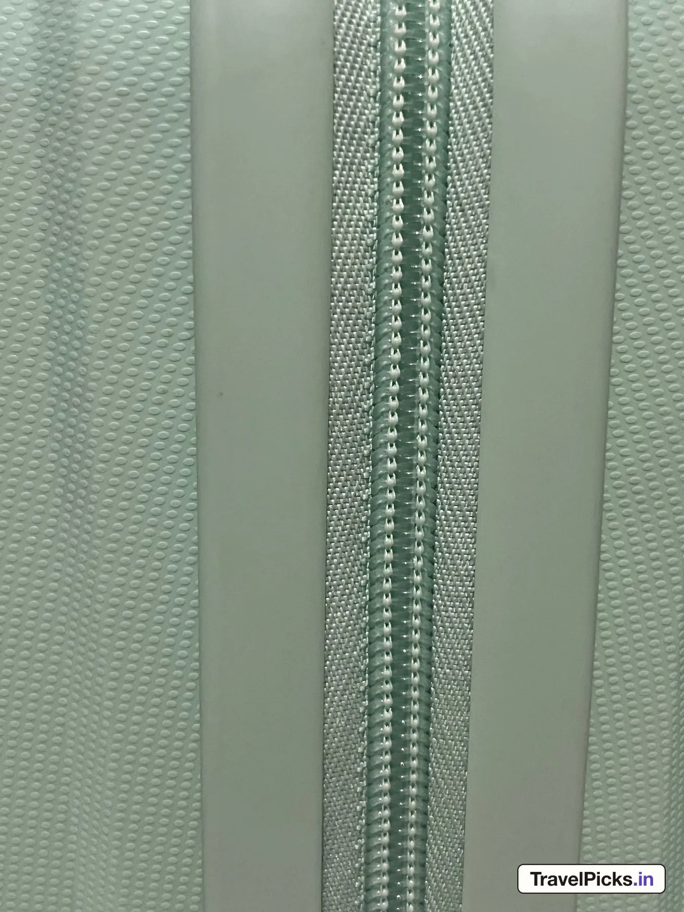 Close view of the closed zip: a mint coil chain on woven mint tape, between two smooth lips of the shell.